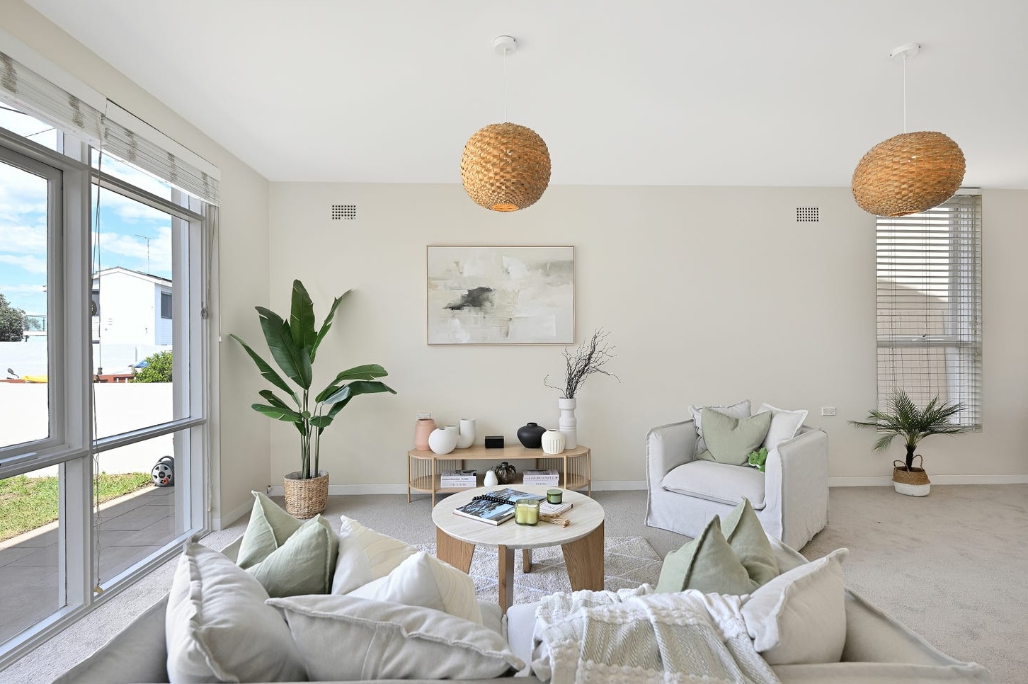 Staged front living room in a Maroubra beach house: linen sofas, armchair, round oak coffee table, abstract art, woven pendants