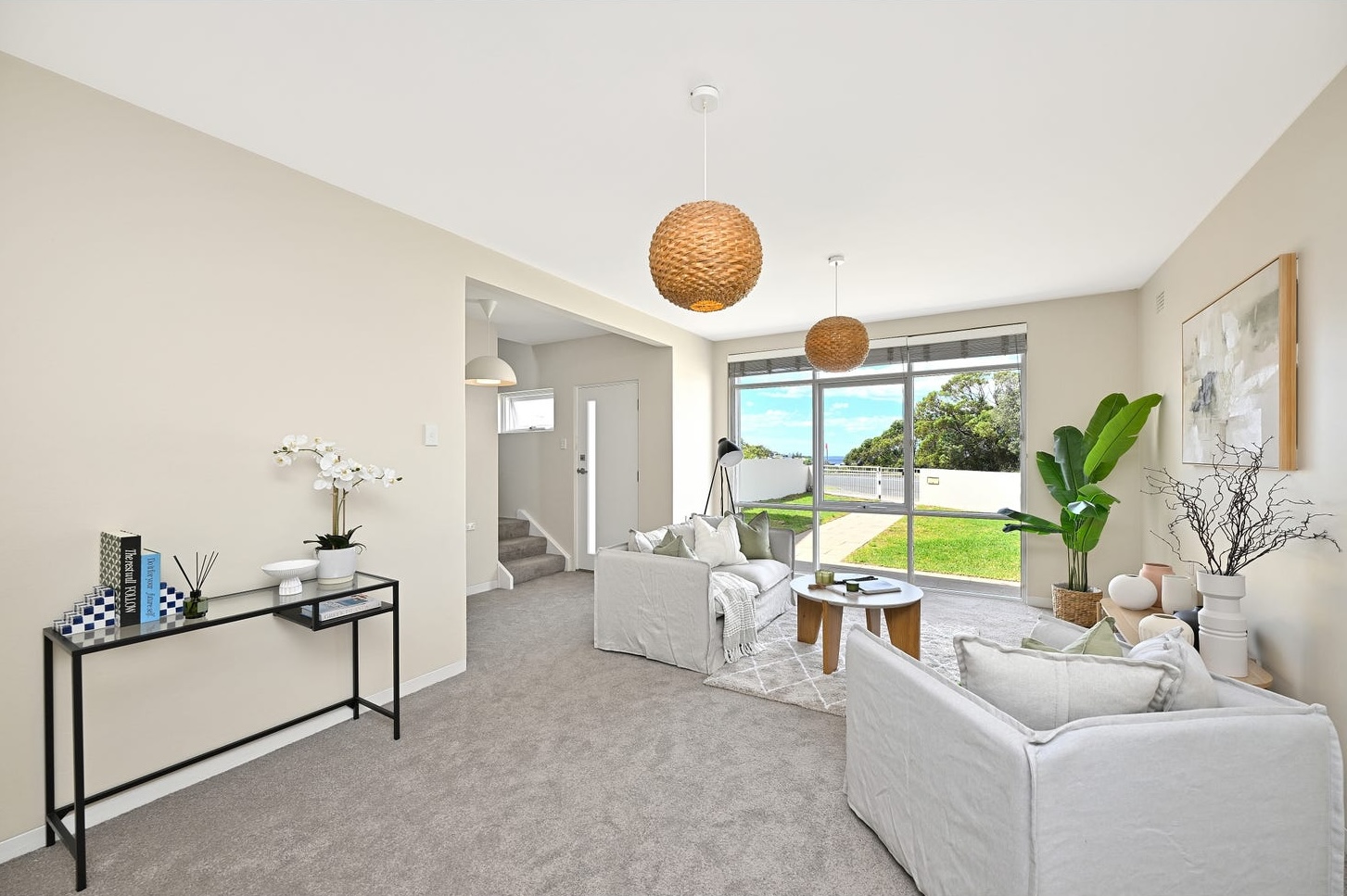 Front living room with floor-to-ceiling glass facing Arthur Byrne Reserve, linen sofas and a black-and-glass console by the stairs