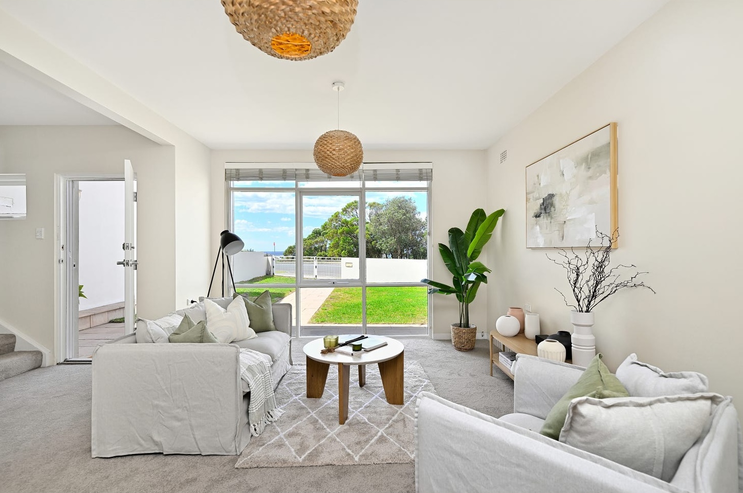 Two slipcovered linen sofas around a round coffee table beside the glass wall of a staged Maroubra house