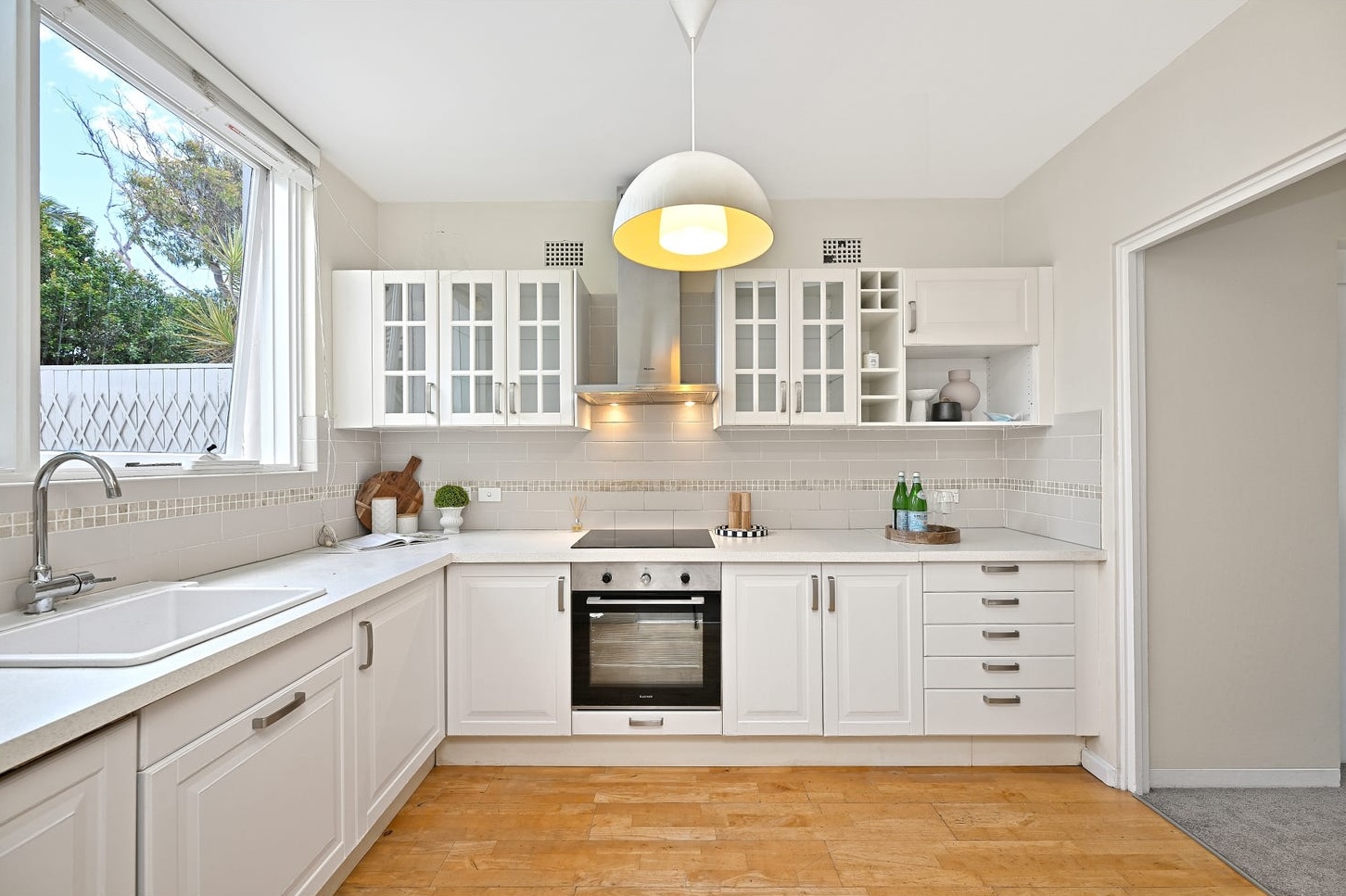 Separate white shaker kitchen with glass-fronted cabinets, lightly styled with a timber board, topiary and a tray