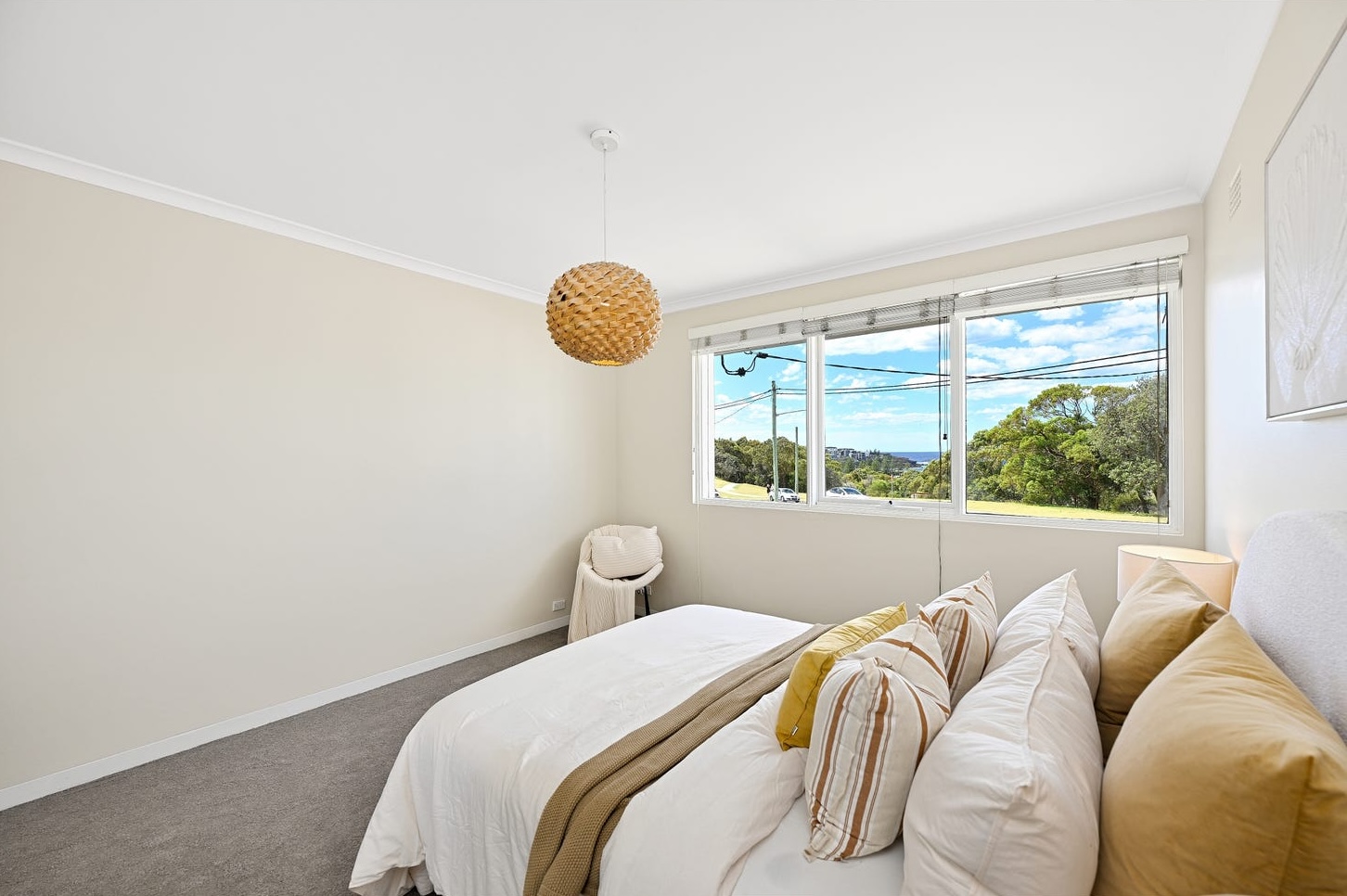 Master bedroom styled with ochre and striped cushions, window looking across the reserve to the ocean at Maroubra
