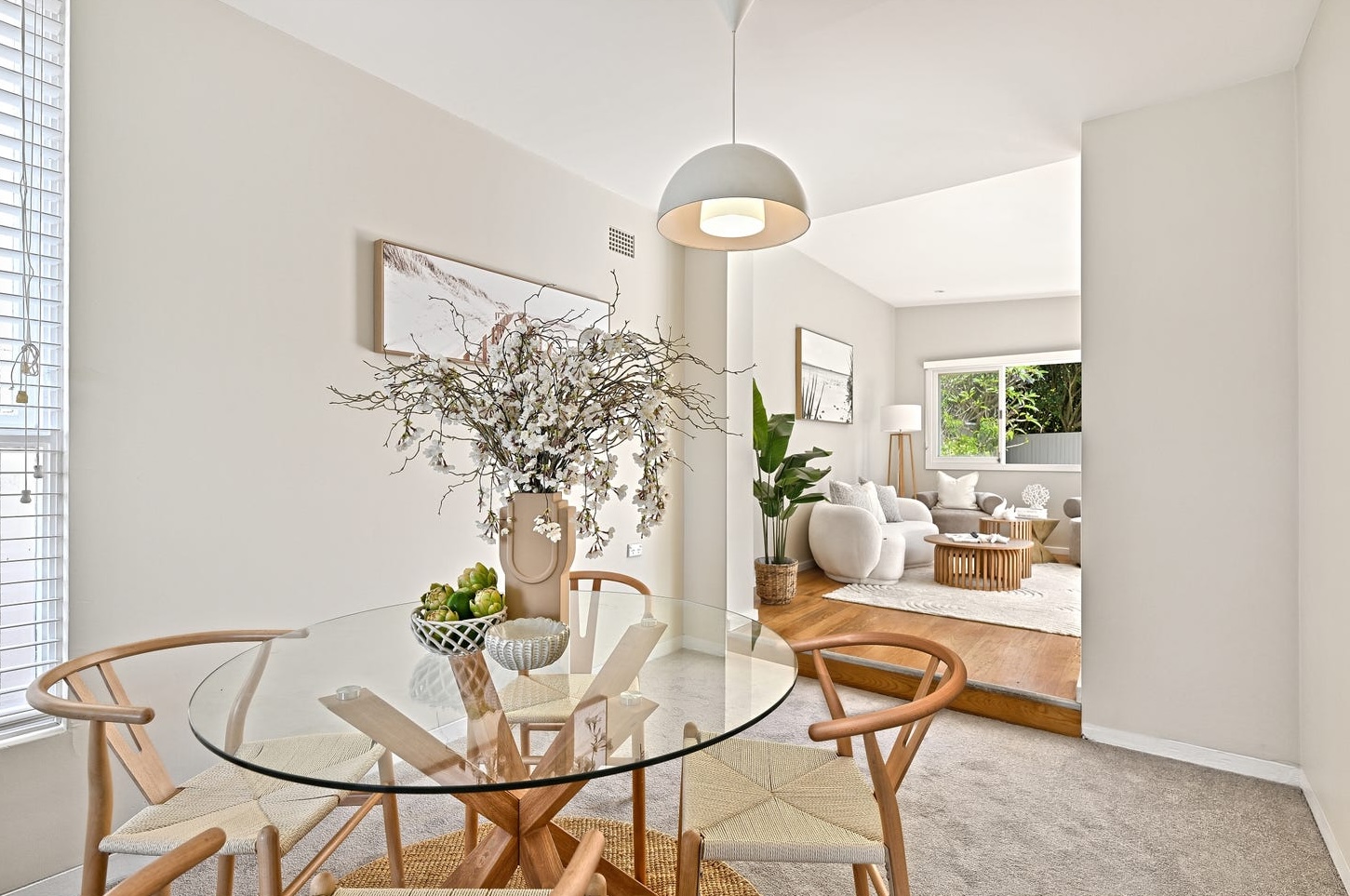 Round glass dining table with wishbone chairs and white blossom branches, one step up to the rear living room