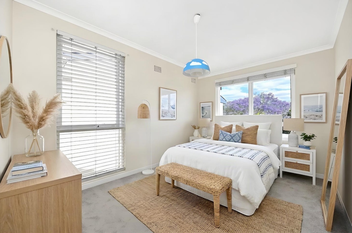 Second bedroom with white bed, navy striped throw, rattan bedside tables and a jacaranda outside the window