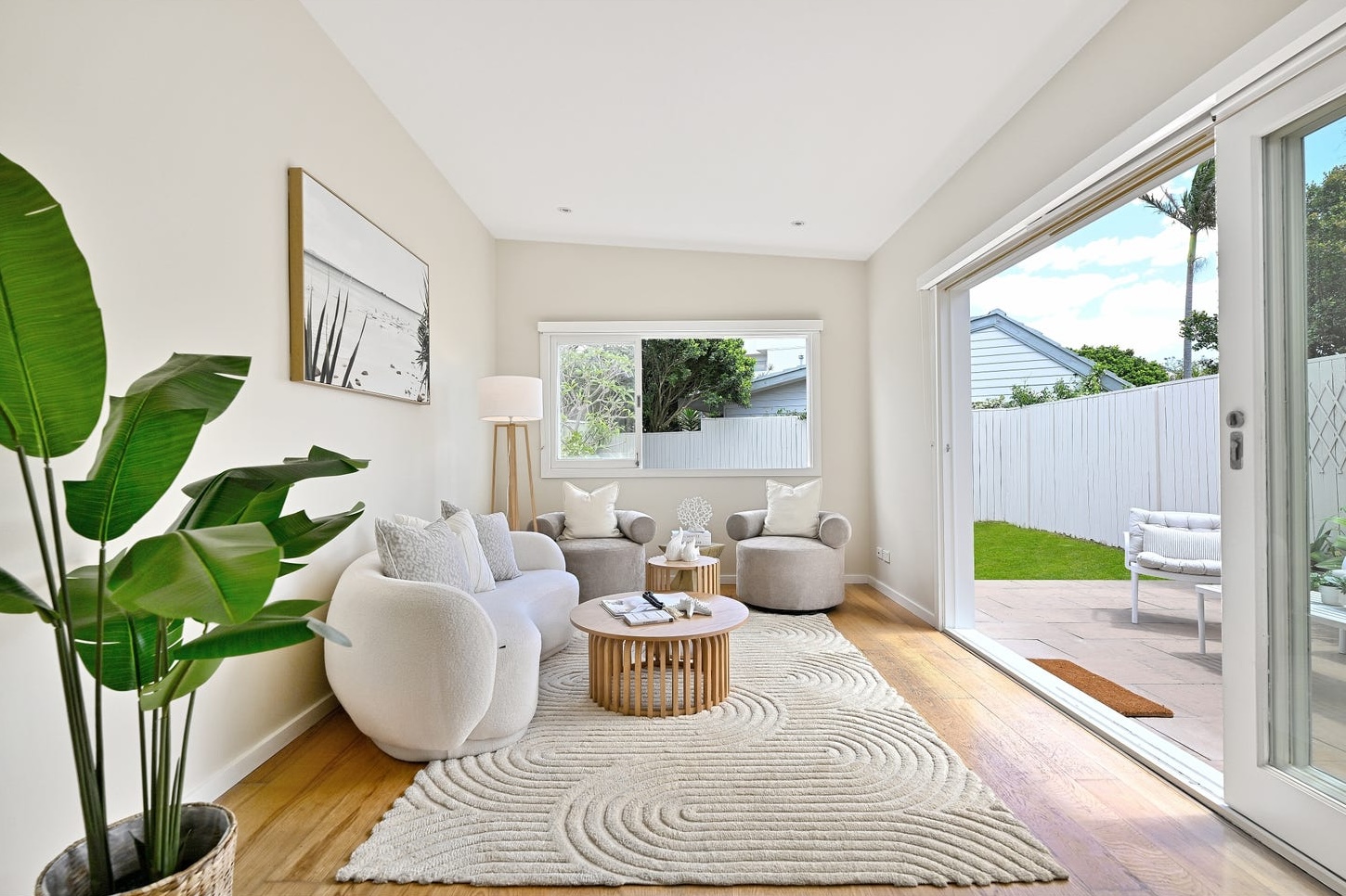 Rear living room in the pavilion: curved boucle sofa, barrel chairs, slatted oak coffee table, doors open to the terrace