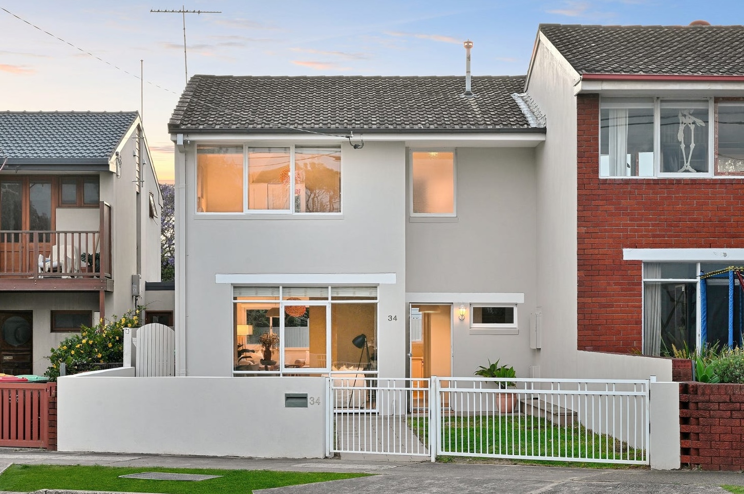 Two-storey house on Broome Street, Maroubra, at dusk with the staged front living room lit behind the glass